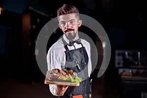 Friendly garcon carries plate with prepared dish in the restaurant.