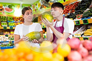 Friendly guy seller helps a girl buyer choose a melon