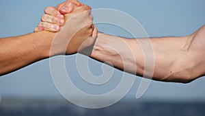 Friendly handshake of two unrecognizable muscular white men on blue sky background. Shaking of male arms outdoor. Two