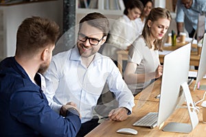 Friendly happy employee handshaking colleague at workplace thanking for help