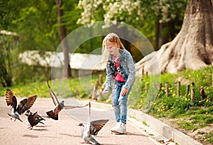 Friendly joyful girl child feeds pigeons in city summer park