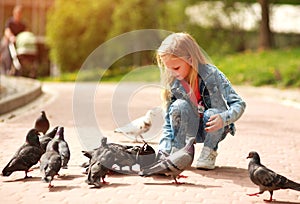 Friendly joyful girl child feeds pigeons in city summer park