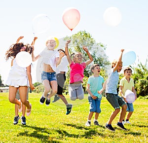 Friendly kids with balloons jumping together in park on summer