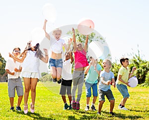 Friendly kids with balloons jumping together in park on summer