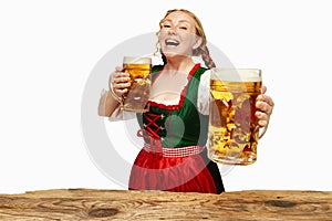 Friendly laughing woman wearing folk German dirndl with two beer mugs over white background. Holiday event, Oktoberfest