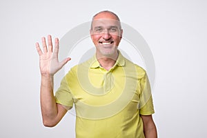 Friendly-looking attractive european man waiving hand in hello gesture while smiling cheerfully.