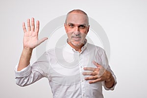 Friendly-looking attractive european man waiving hand in hello gesture while smiling cheerfully.