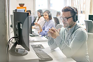 Friendly male call centre operator listening to a client while working in group with other customer support agents.