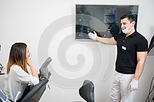 Friendly male dentist showing to female patient her dental x-ray image on computer monitor in a dental clinic