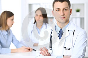 Friendly male doctor on the background with patient and her physician in hospital office