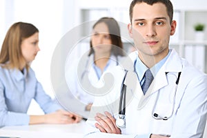 Friendly male doctor on the background with patient and her physician in hospital office