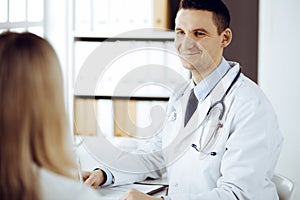 Friendly male doctor and patient woman discussing current health examination while sitting in sunny clinic. Perfect