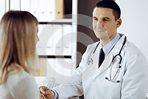 Friendly male doctor and patient woman discussing current health examination while sitting in sunny clinic. Perfect