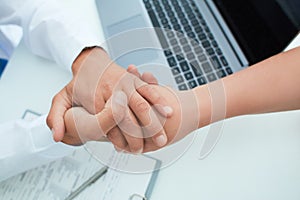 Friendly male doctor`s hands holding female patient`s hand for encouragement and empathy. Partnership, trust and medical