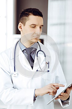 Friendly male doctor using tablet computer in sunny clinic. Medicine and healthcare concept