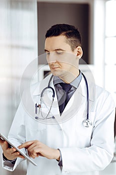 Friendly male doctor using tablet computer in sunny clinic. Medicine and healthcare concept