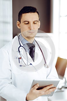 Friendly male doctor using tablet computer in sunny clinic. Medicine and healthcare concept