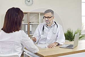 Friendly male medical specialist discussing diagnosis with his female patient in medical office.