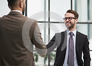 Friendly male professional colleagues greeting handshaking meeting in company office hall