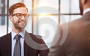 Friendly male professional colleagues greeting handshaking meeting in company office hall