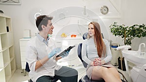 Friendly man dentist with digital talking with female patient during appointment in dental clinic