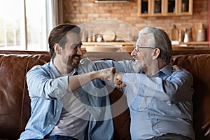 Friendly mature grandfather and young adult grandson give fist bump