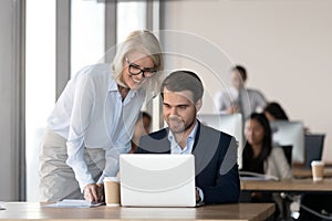 Friendly mentor training employee in office helping with computer work