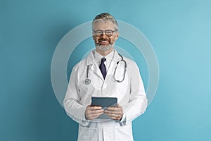 Friendly middle aged doctor holding digital tablet, copy space