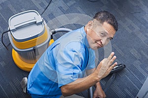 A friendly middle-aged janitor in a blue uniform making the ok sign confirming that the vacuum cleaner works. Employed at an