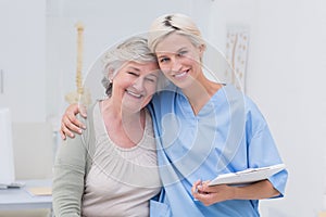 Friendly nurse with arm around senior patient in clinic