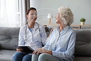 Friendly nurse laughing with elderly female patient during homecare visit