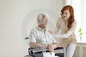Friendly nurse supporting smiling paralyzed senior man in a whee