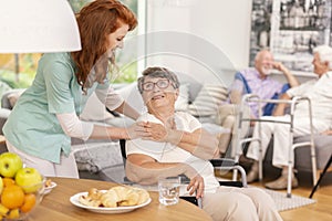 Friendly nurse supporting smiling senior woman in nursing house.