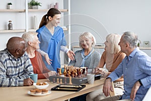 Friendly nurse talking to elderly people playing table games