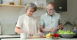 Friendly older age spouses talk while preparing breakfast at kitchen