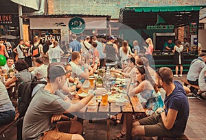 Friendly party with crowd of eating people at table during outdoor Street Food Festival