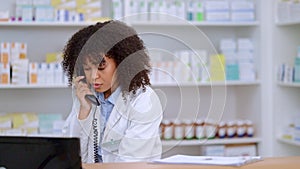 Friendly pharmacist talking on a phone call and checking something on her computer in a pharmacy. Woman using pc to