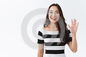 Friendly, pleasant and cheerful east-asian woman in striped t-shirt raising palm, wave hand greeting, saying hi or hello