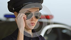 Friendly police lady taking off sunglasses, looking to camera and smiling, duty