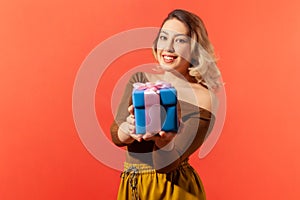 Friendly positive woman holding blue gift with pink ribbon, preparing present for you, looking at camera with smile