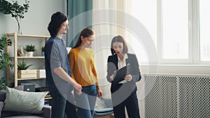 Friendly realtor talking to clients man and woman showing papers in new house