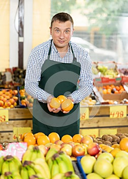 Friendly salesman offering ripe oranges in fruits and vegetables store