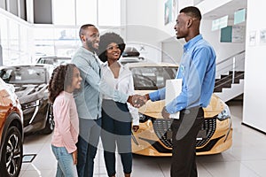 Friendly salesman shaking hands with Afro family, making car purchase agreement at auto dealership