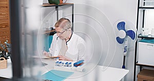 Friendly senior Caucasian doctor woman in lab coat, eyeglasses smiles consulting remote patient using laptop webcam chat