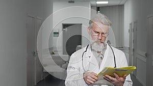 Friendly senior doctor smiling to the camera standing at hospital hallway