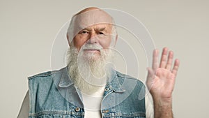 Friendly Senior Man Waving Hello in Denim Vest, Grey Background