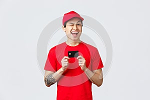 Friendly smiling asiand elivery man in red cap and t-shirt uniform, wink cheerful, recommend using credit card, buy