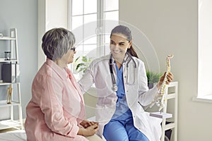 Friendly, smiling doctor talking to senior patient and showing anatomical backbone model
