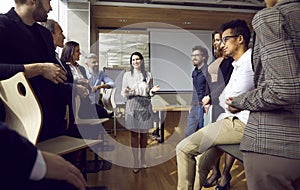 Friendly smiling female business coach talking to group of people standing in office around her.