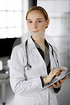 Friendly smiling female doctor using clipboard in clinic. Portrait of friendly physician woman at work place. Perfect